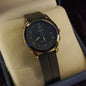 Luxury watch with black strap and gold case on a textured surface by Janxy Jewels